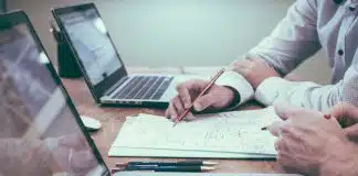 person holding pencil near laptop computer