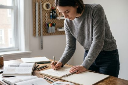 Étudiante en design travaillant sur des croquis géométriques dans son appartement, entourée de livres et de swatches de couleurs